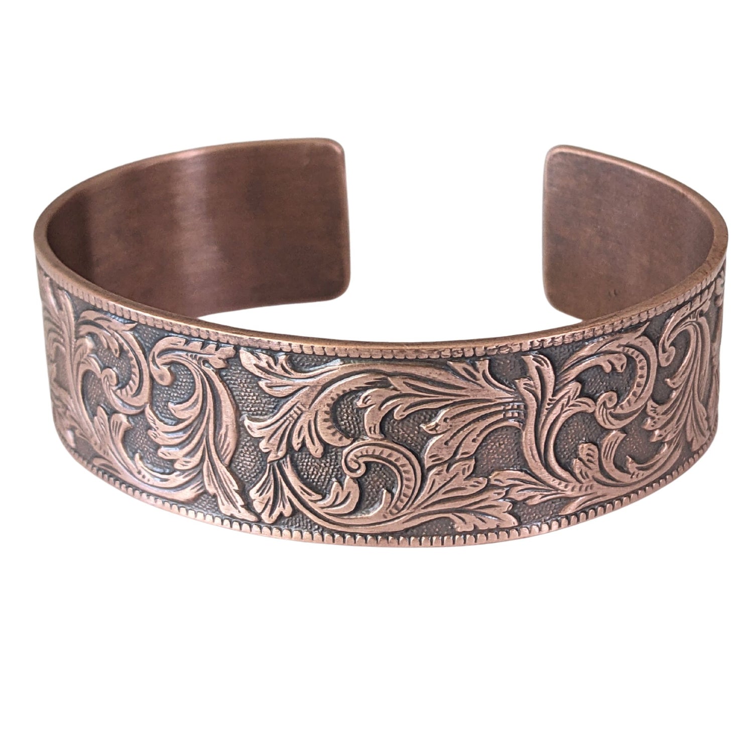 copper cuff bracelet with a repeating flourish leaf pattern on a spotted texture background.