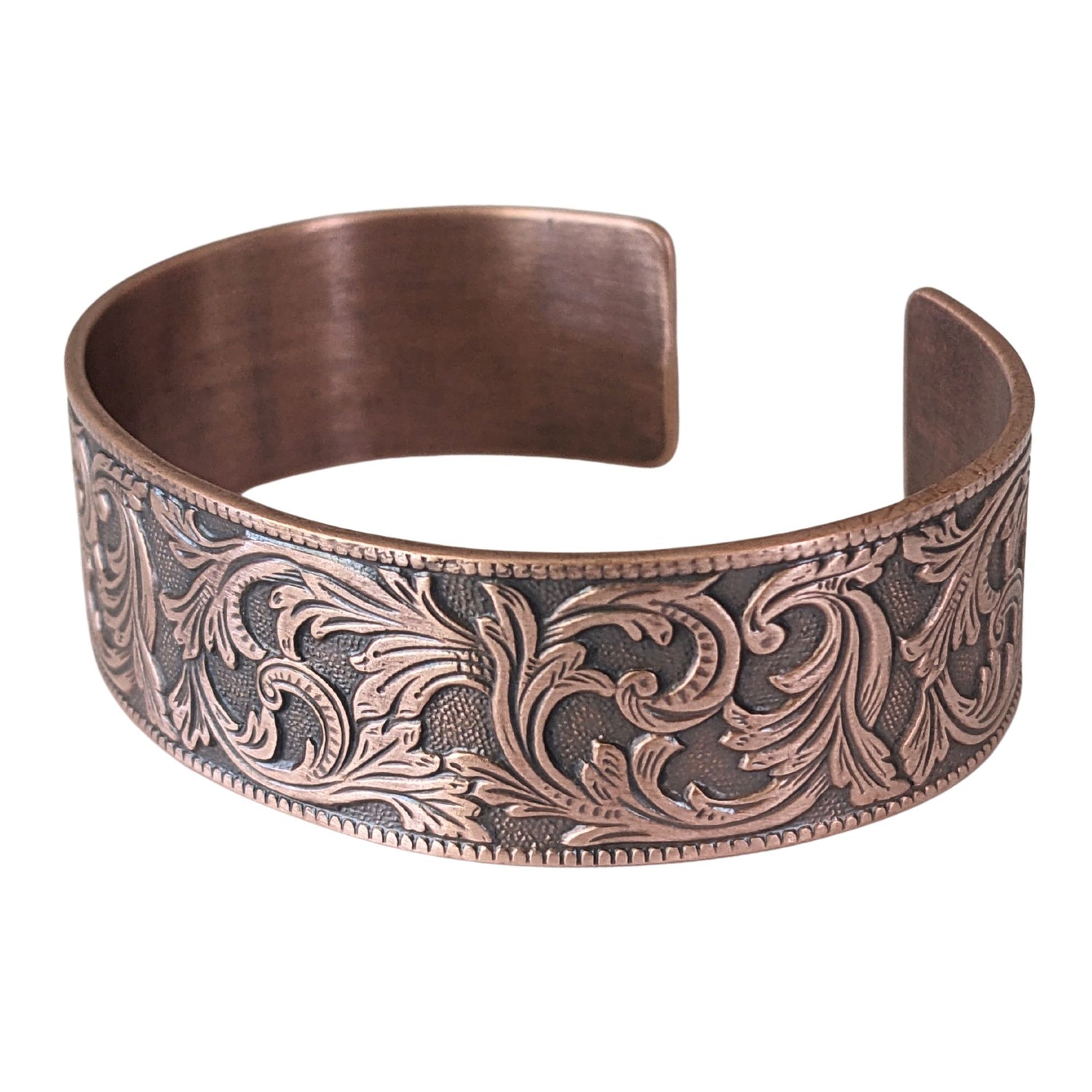 copper cuff bracelet with a repeating flourish leaf pattern on a spotted texture background.
