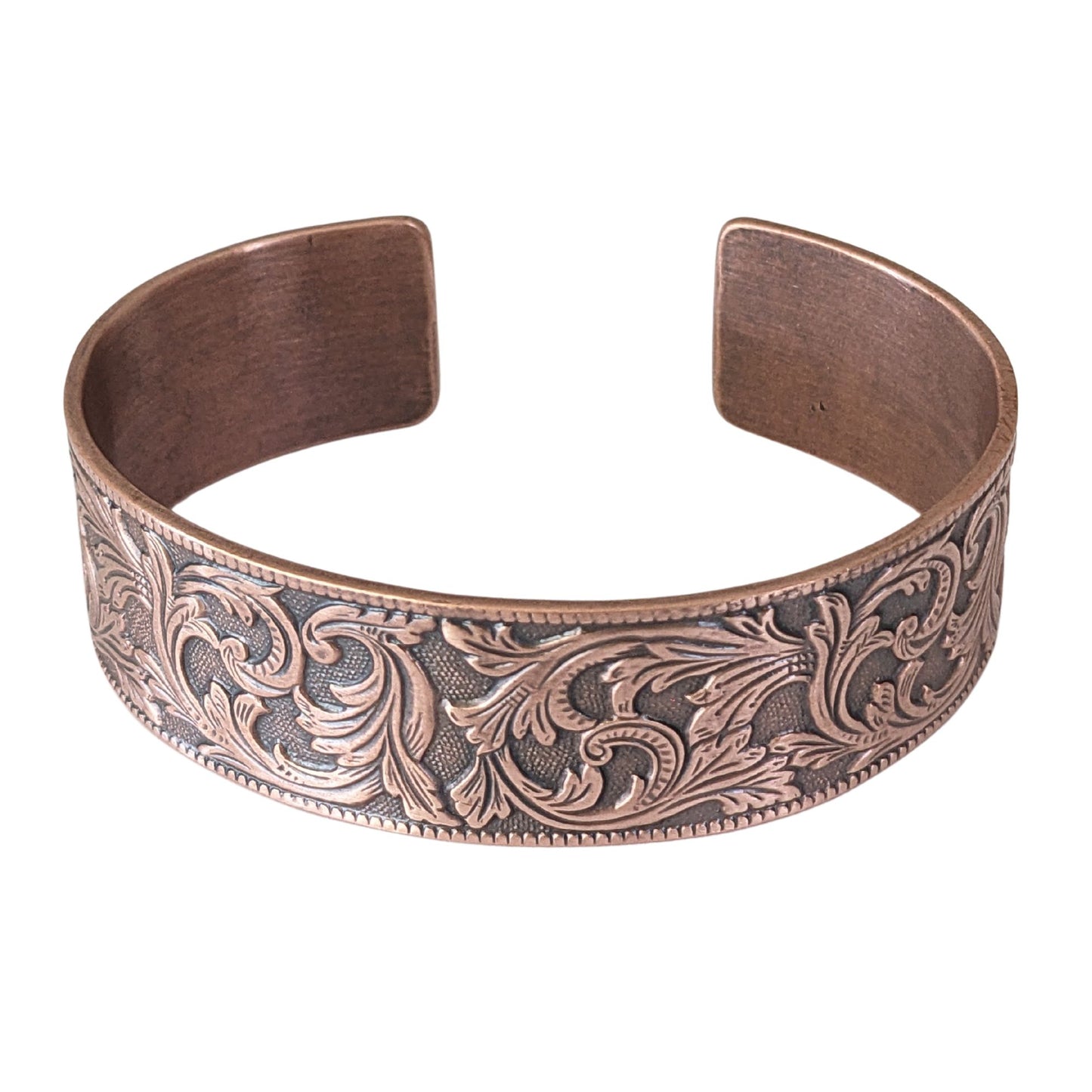 copper cuff bracelet with a repeating flourish leaf pattern on a spotted texture background.
