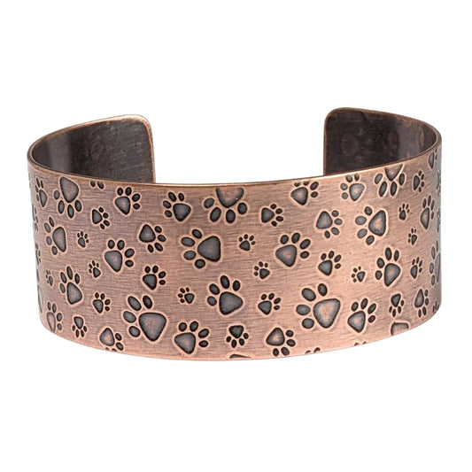 Copper cuff bracelet covered in a dog paw print design. The paw prints are in various sizes.