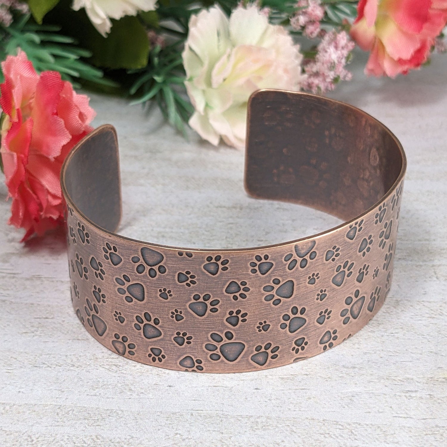 Copper cuff bracelet covered in a dog paw print design. The paw prints are in various sizes.