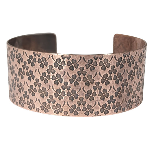 Copper cuff bracelet covered in impressions of small four leaf clovers.