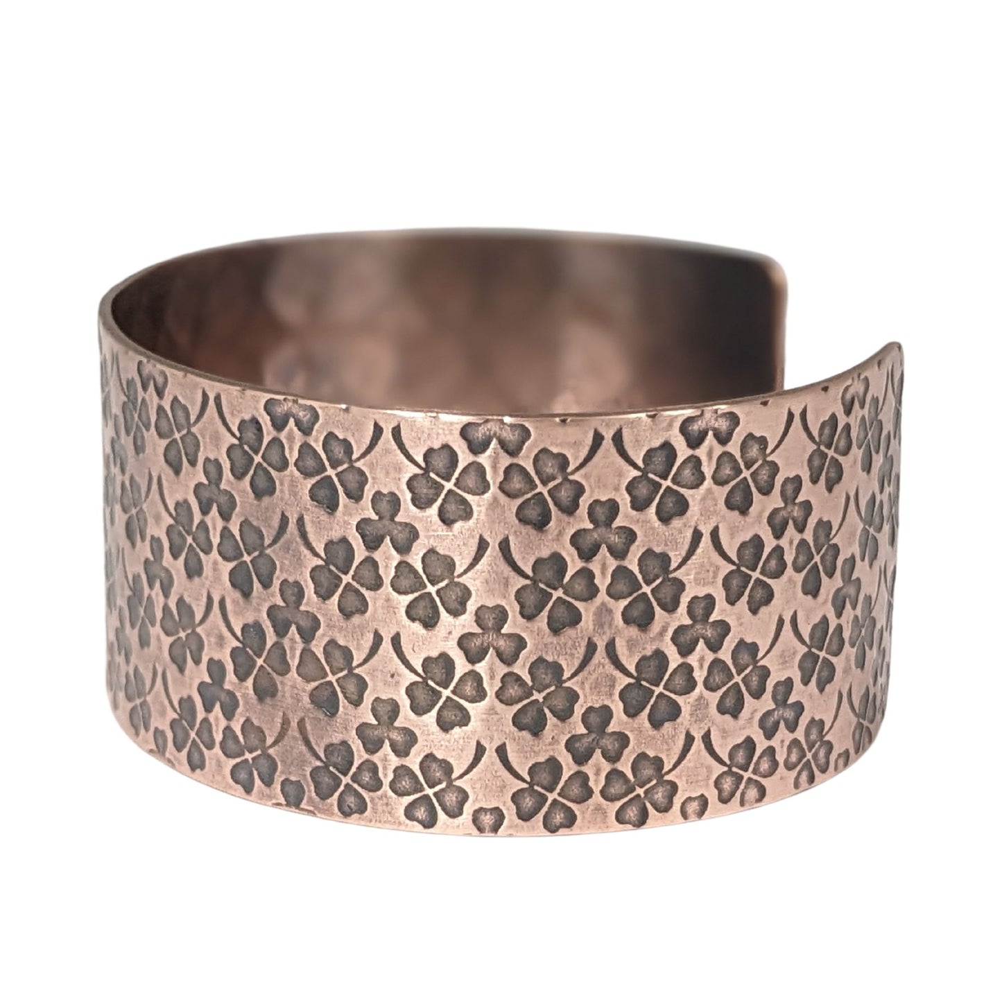 Copper cuff bracelet covered in impressions of small four leaf clovers.