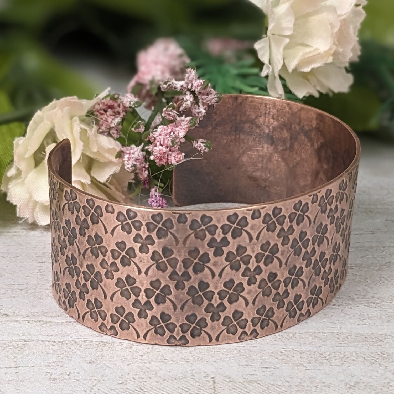 Copper cuff bracelet covered in impressions of small four leaf clovers.