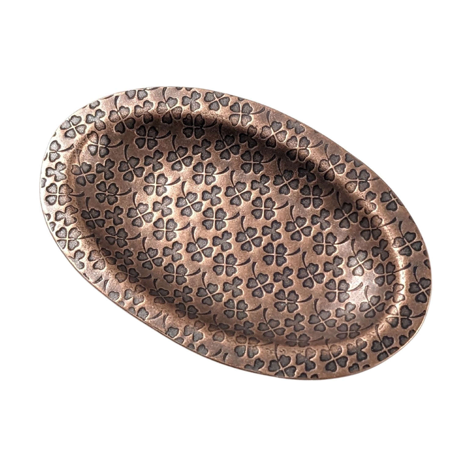 An oval copper ring dish with a raised edge. The dish has an impressed pattern of four leaf clovers.