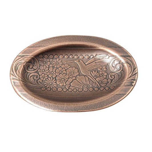 Oval copper ring dish with a raised lip. Pattern across middle is a hummingbird surronded by flowers. The edge of the pattern is a scrolled leaf resembling ferns.