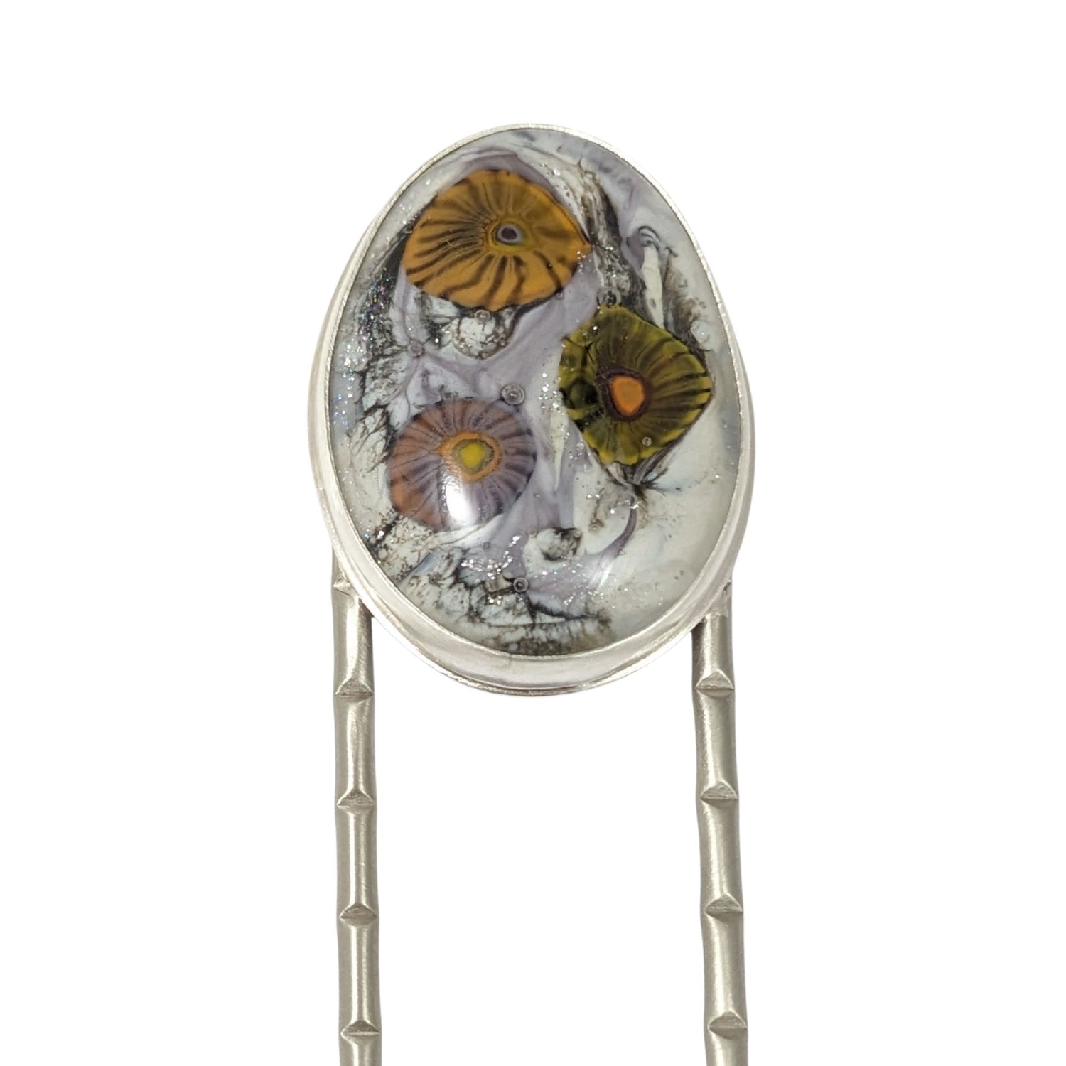 Lampwork glass oval with three abstract flowers in yellow, green, and pale purple set on a nickel hair fork.