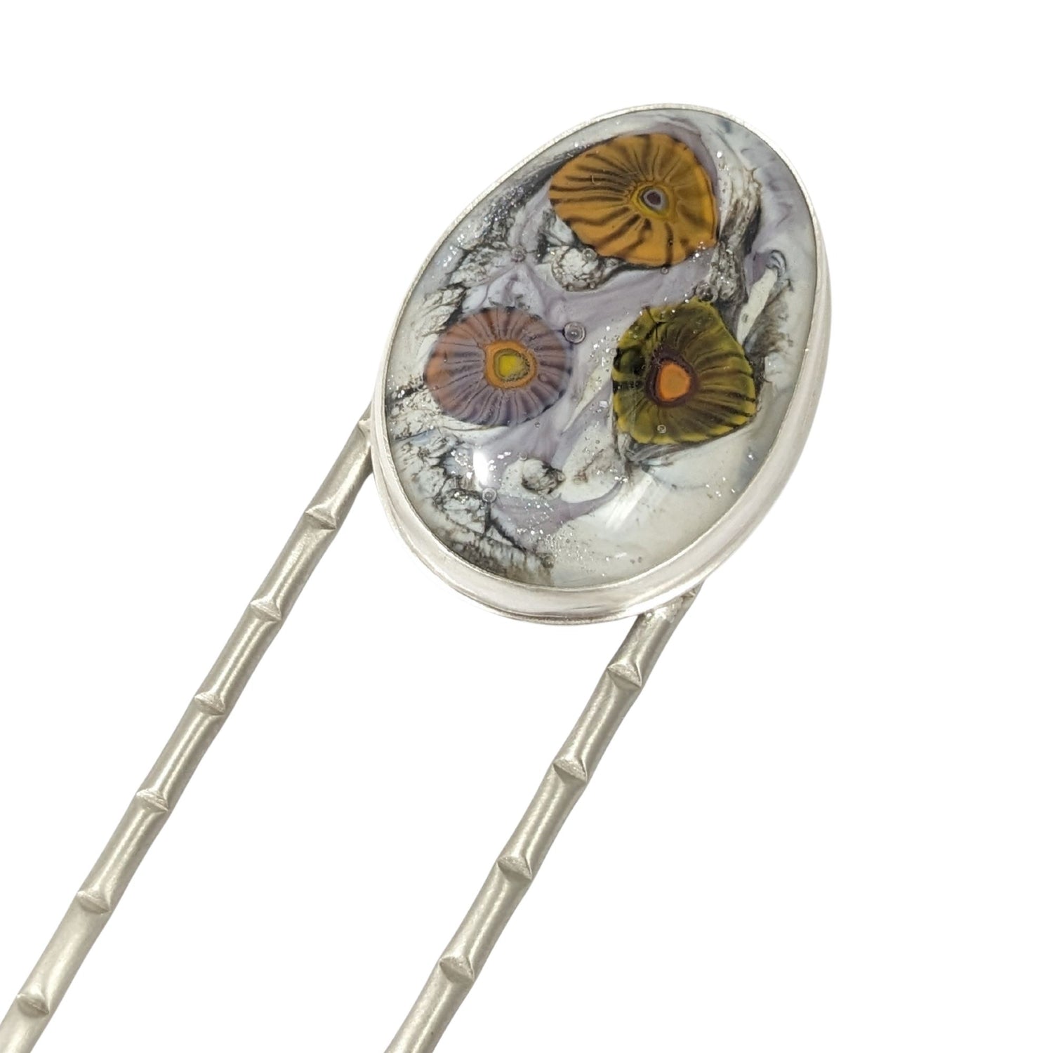 Lampwork glass oval with three abstract flowers in yellow, green, and pale purple set on a nickel hair fork.