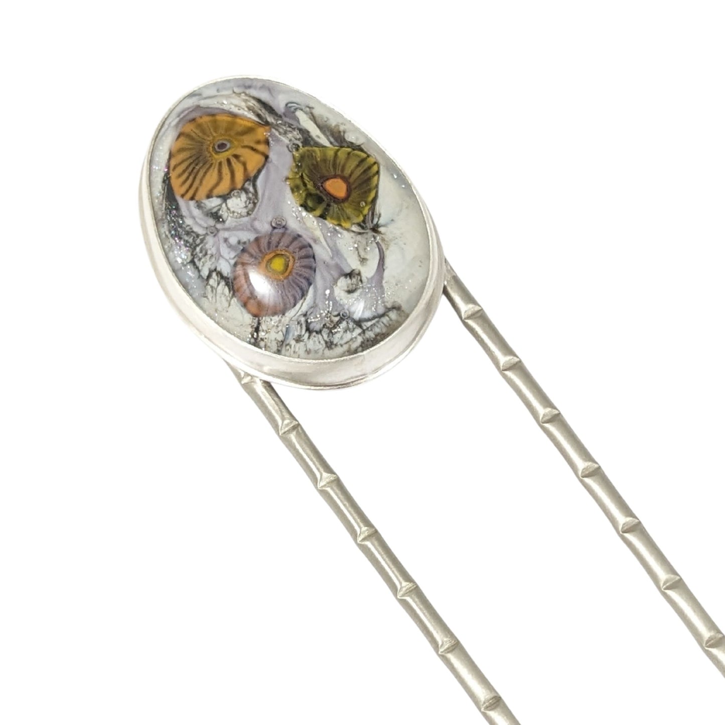 Lampwork glass oval with three abstract flowers in yellow, green, and pale purple set on a nickel hair fork.