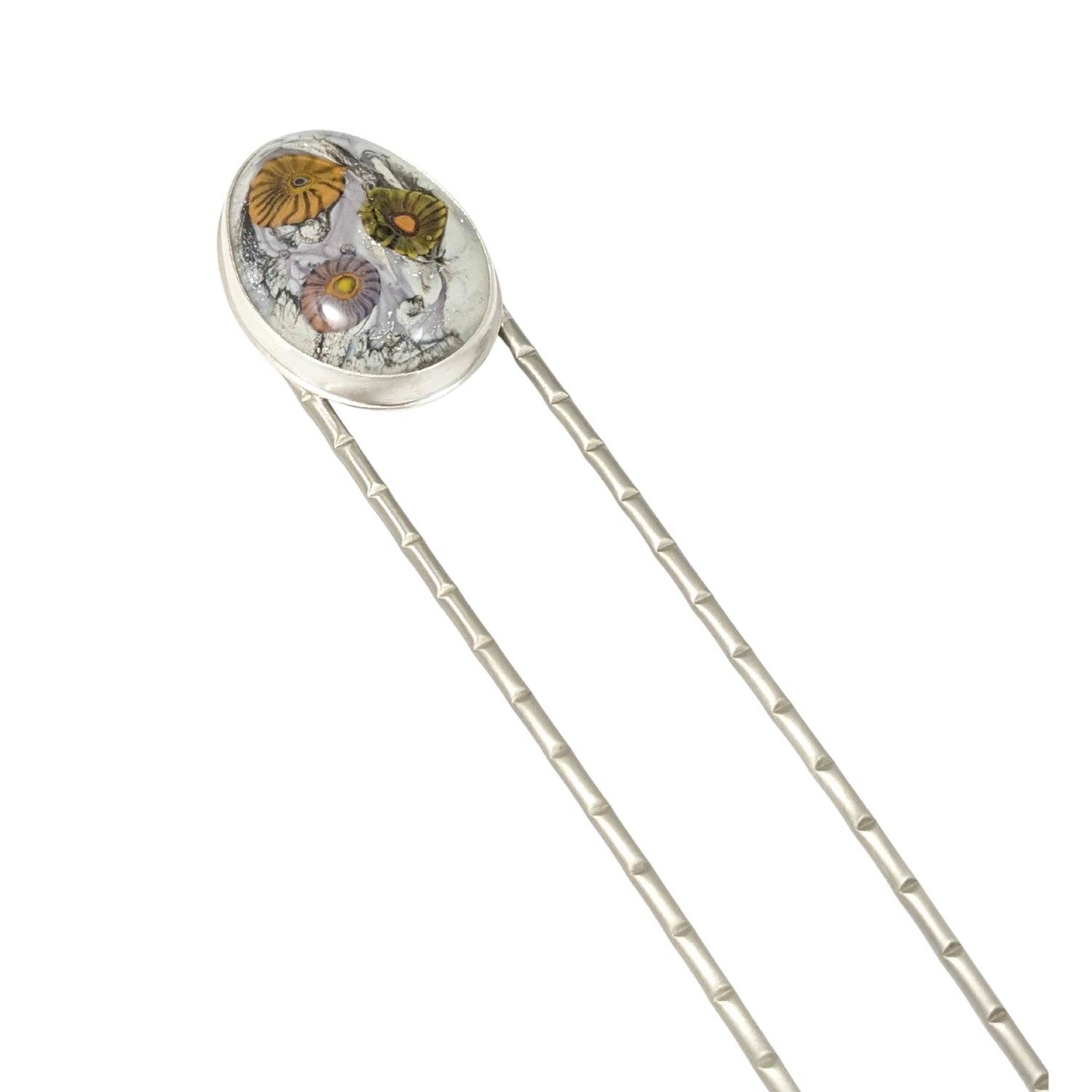 Lampwork glass oval with three abstract flowers in yellow, green, and pale purple set on a nickel hair fork.