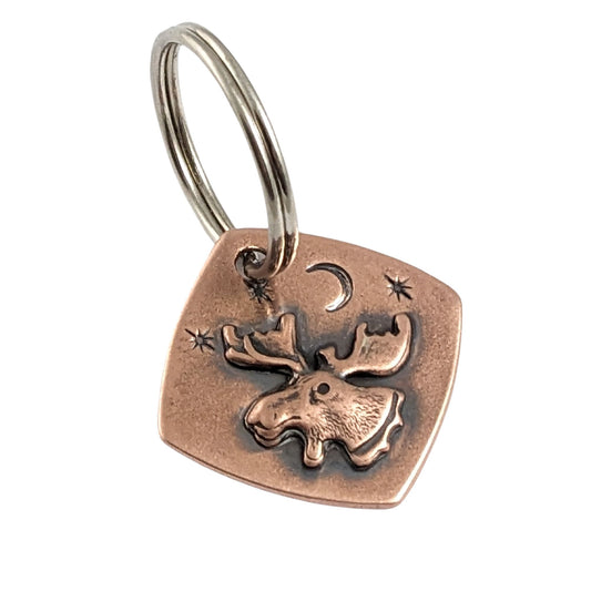 square copper keychain with raised moose head, background is a moon and stars