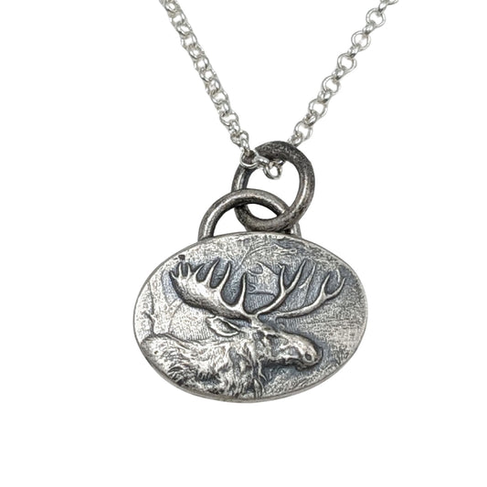 Oval silver pendant with a raised design of a moose, most of the body and all of the head and antlers.