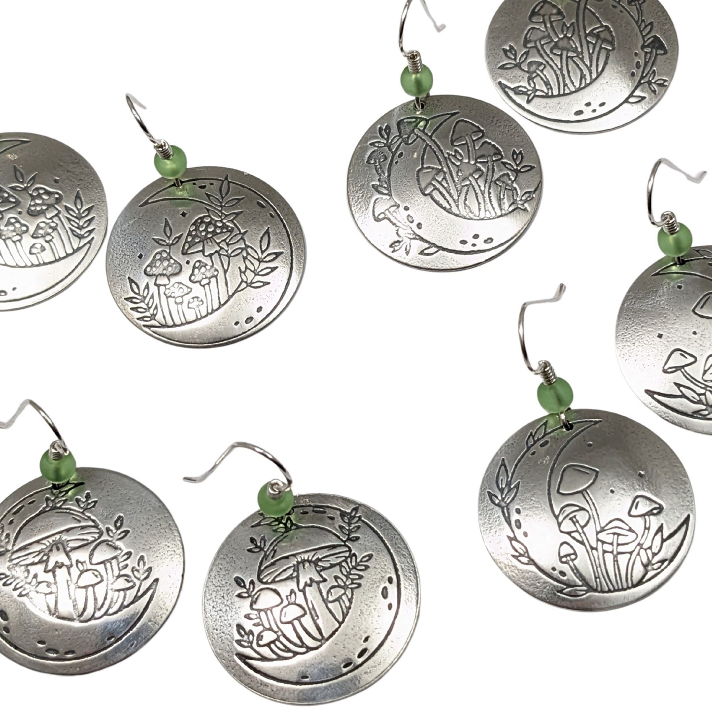 A set of domed sterling silver round drop earrings featuring an engraved mushroom and crescent moon design, accented with small green beads and silver ear wires.