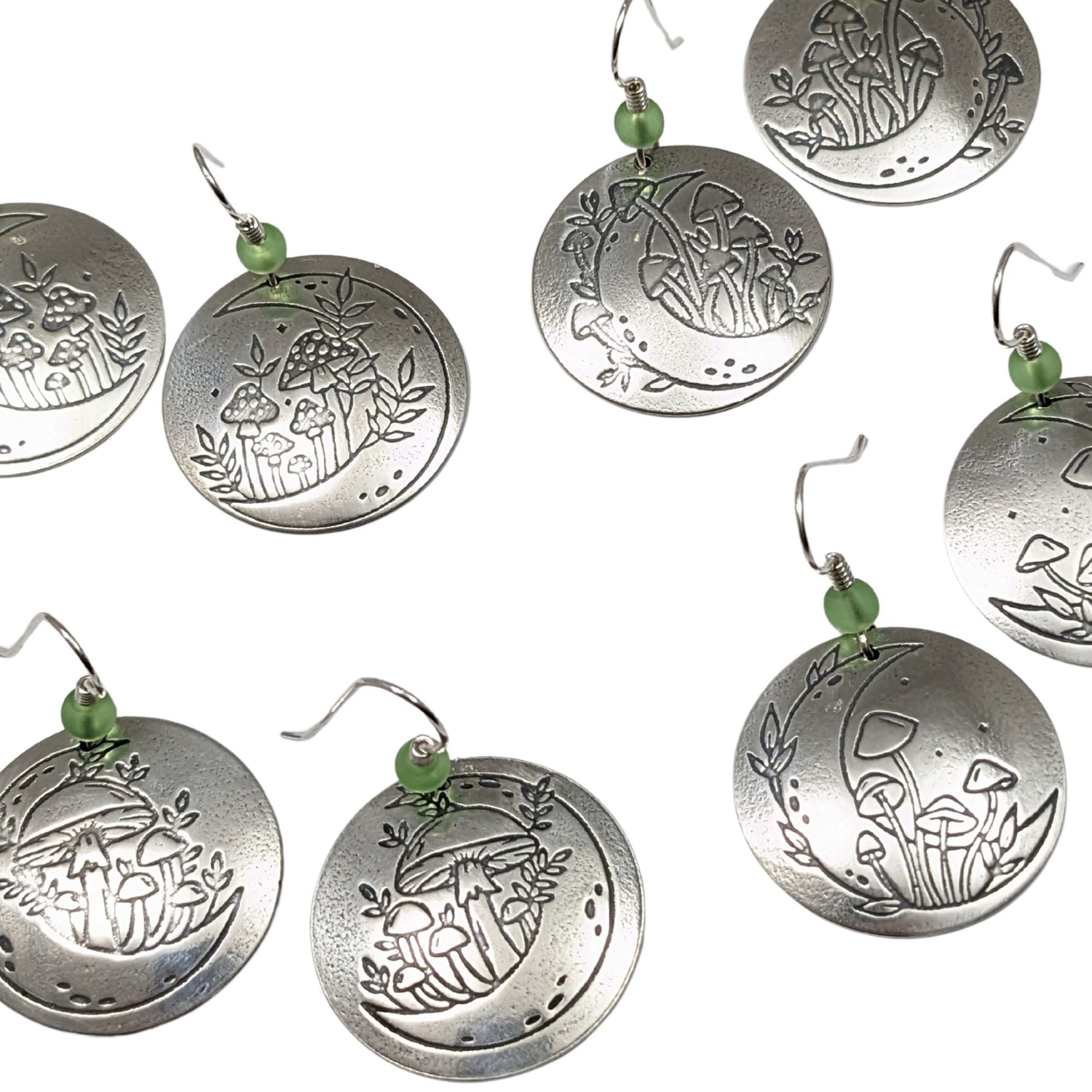 A set of domed sterling silver round drop earrings featuring an engraved mushroom and crescent moon design, accented with small green beads and silver ear wires.