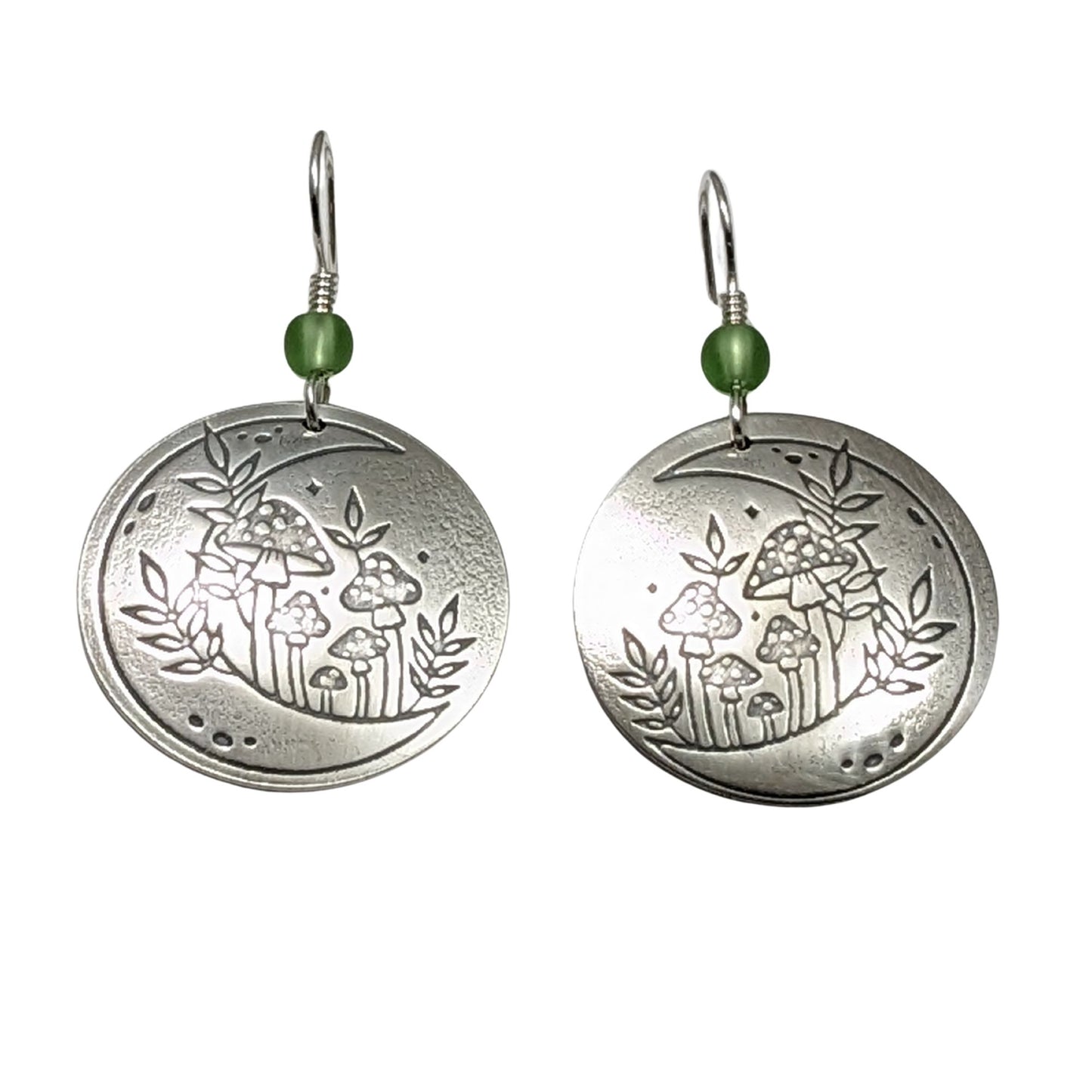 A pair of domed sterling silver round drop earrings featuring an engraved mushroom and crescent moon design, accented with small green beads and silver ear wires.