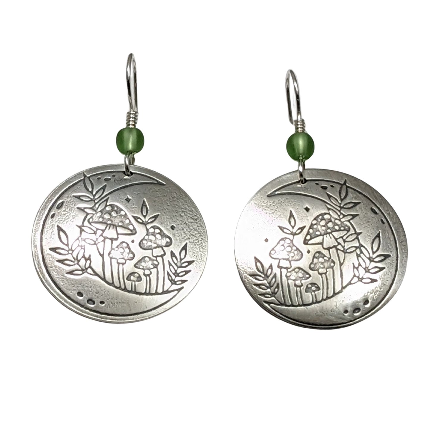 A pair of domed sterling silver round drop earrings featuring an engraved mushroom and crescent moon design, accented with small green beads and silver ear wires.