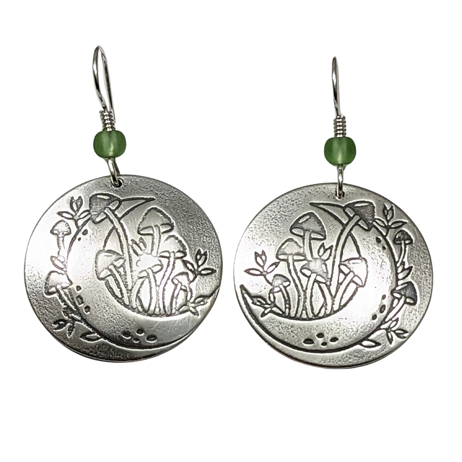 A pair of domed sterling silver round drop earrings featuring an engraved mushroom and crescent moon design, accented with small green beads and silver ear wires.