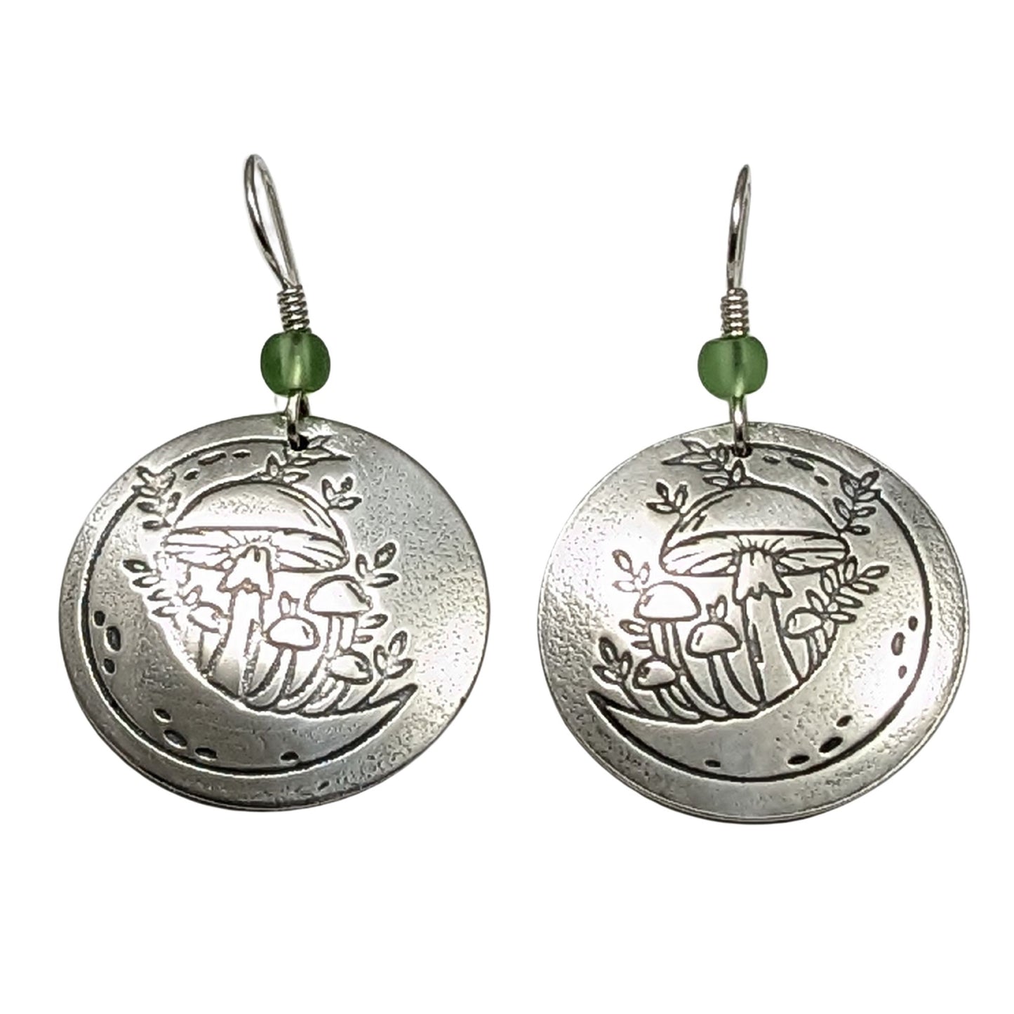 A pair of domed sterling silver round drop earrings featuring an engraved mushroom and crescent moon design, accented with small green beads and silver ear wires.
