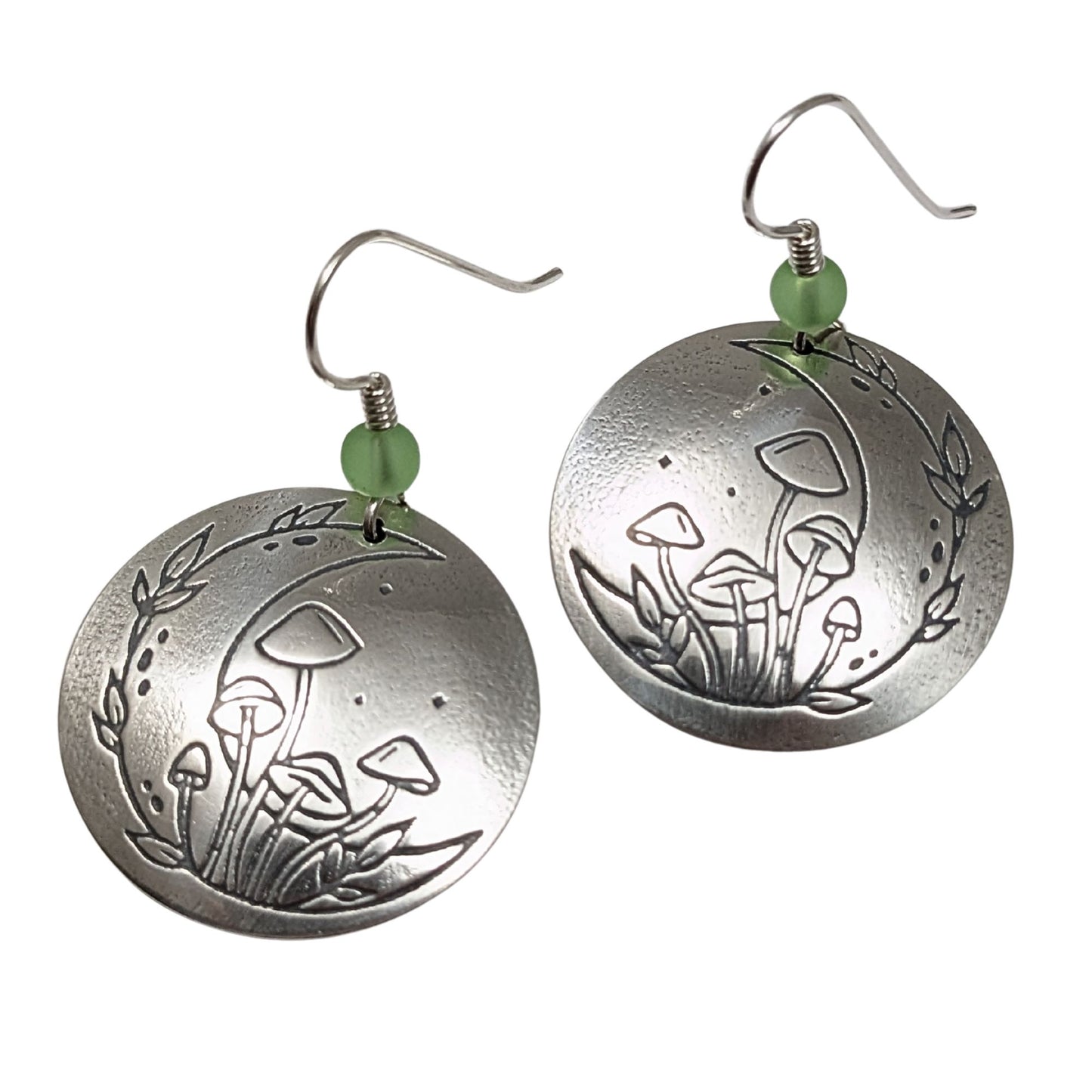 A pair of domed sterling silver round drop earrings featuring an engraved mushroom and crescent moon design, accented with small green beads and silver ear wires.