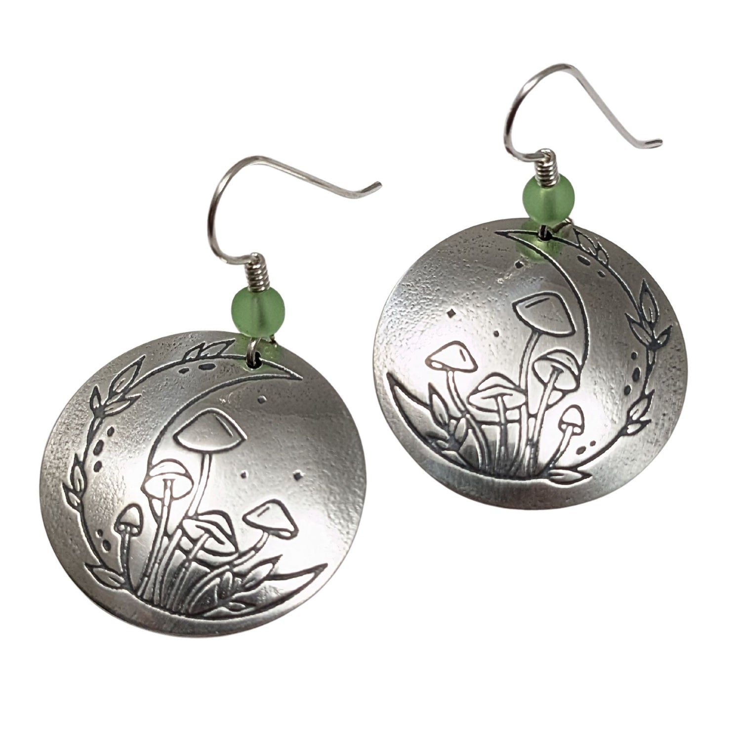 A pair of domed sterling silver round drop earrings featuring an engraved mushroom and crescent moon design, accented with small green beads and silver ear wires.