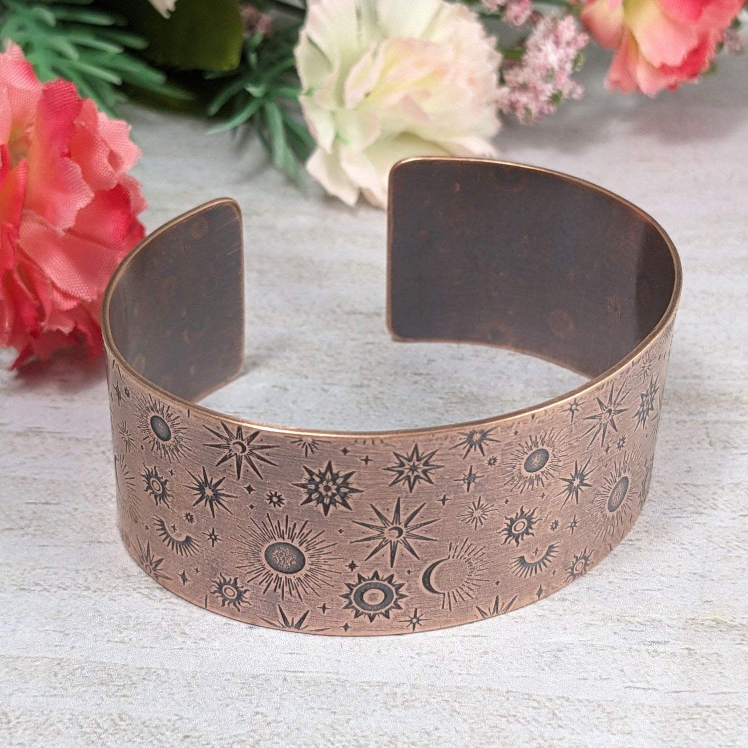 A one inch wide copper cuff bracelet covered in an impressed design of stars and planets.