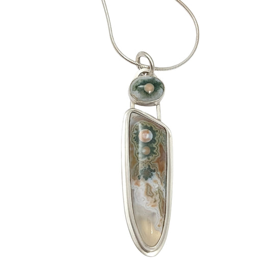 Long narrow sterling silver pendant. The main stone is clear toward the bottom, the rest is whit and orange background with three green cogwheel shaped designs with orange centers. A top accent stone has the same white, green, and orange combination.