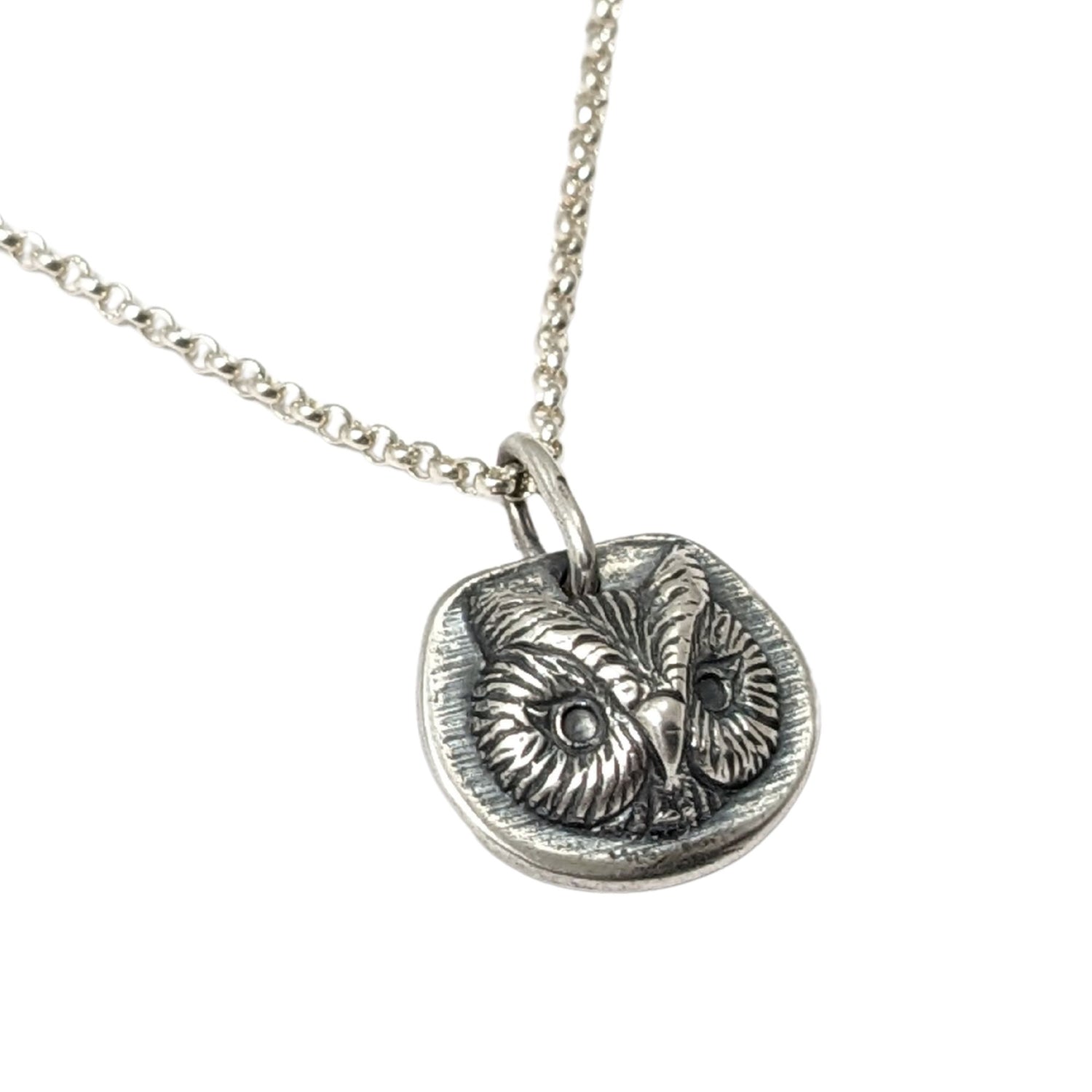 Sterling silver pendant of an owl face. The pendant is three dimensional and thick.