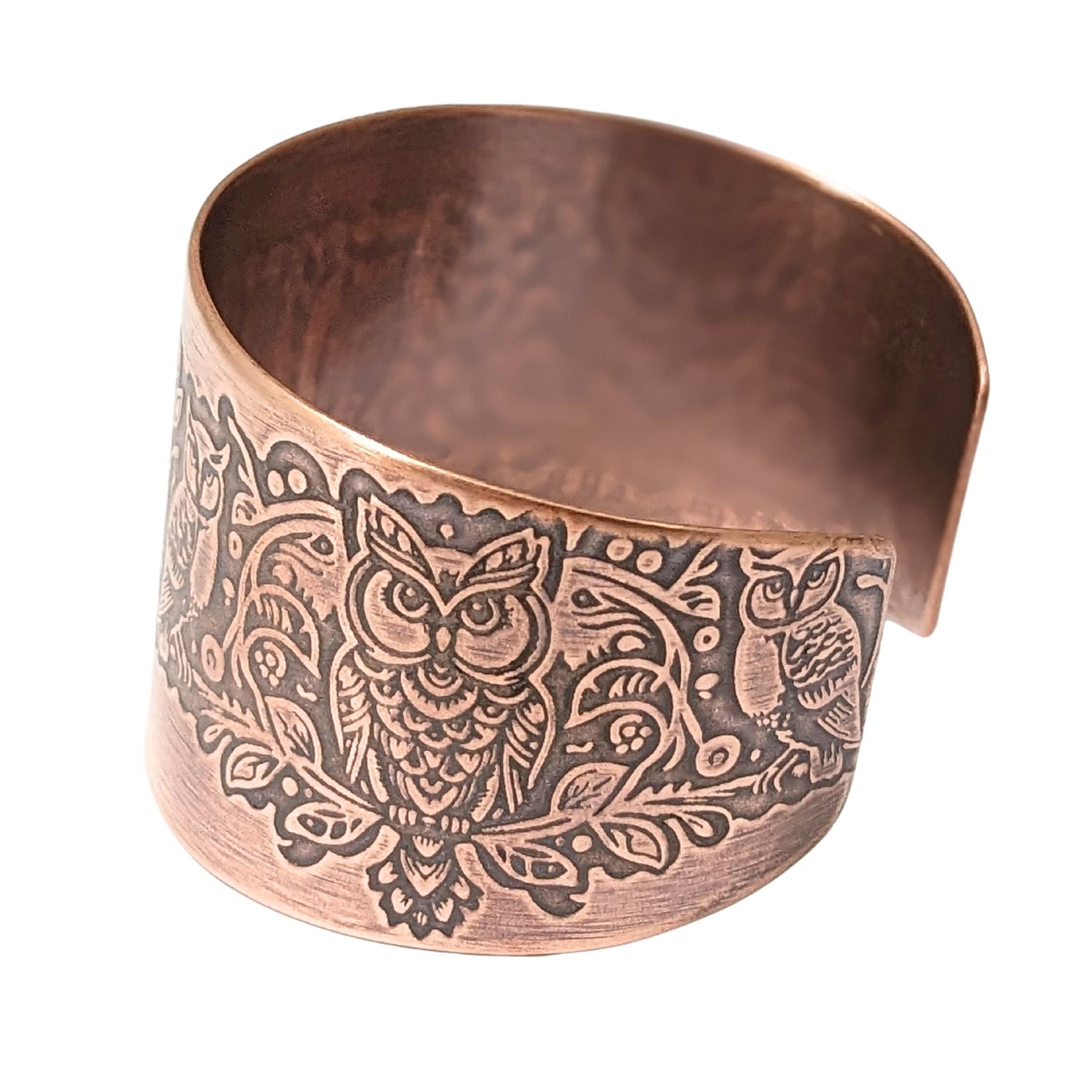 Side detail view of copper cuff bracelet showing a larger owl facing forward. The same owl design is repeated on the other side of the cuff.