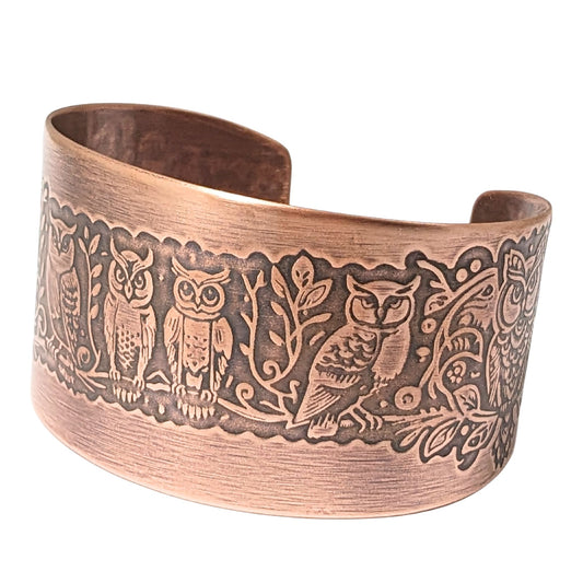 Wide tapered copper cuff bracelet. A design of various owls on a tree branch wraps the entire length of the bracelet.