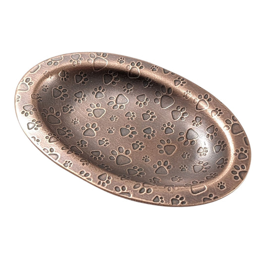An oval copper ring dish with a raised edge. The dish has an impressed pattern of dog paw prints.