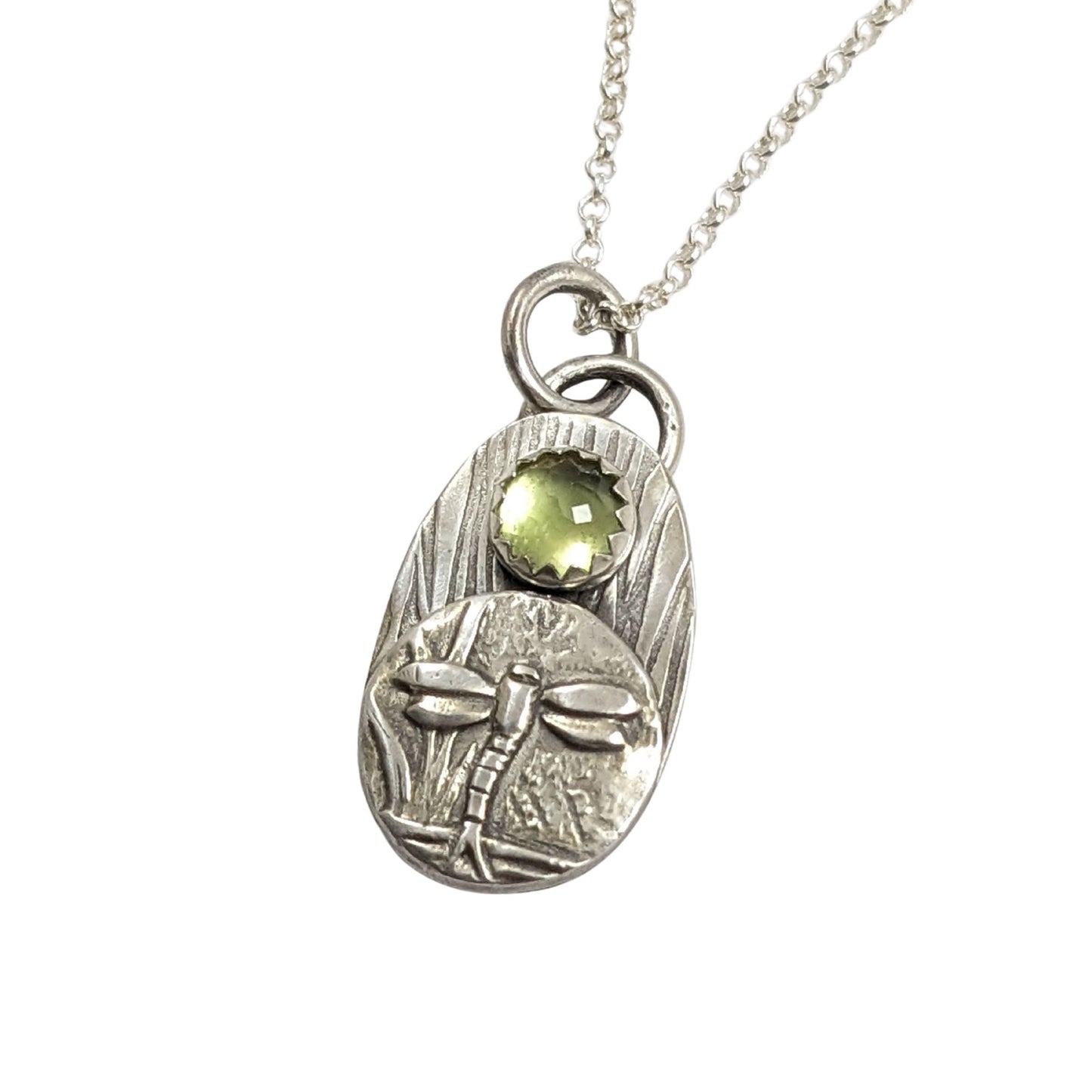 Dragonfly pendant from the set of four sterling silver pendants with pond creatures. each has a reed-textured background and green peridot gemstone. Creatures are wasp, lizard, frog, dragonfly.