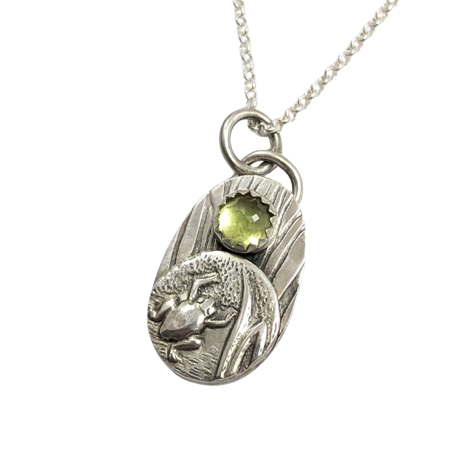 Frog pendant from the set of four sterling silver pendants with pond creatures. each has a reed-textured background and green peridot gemstone.