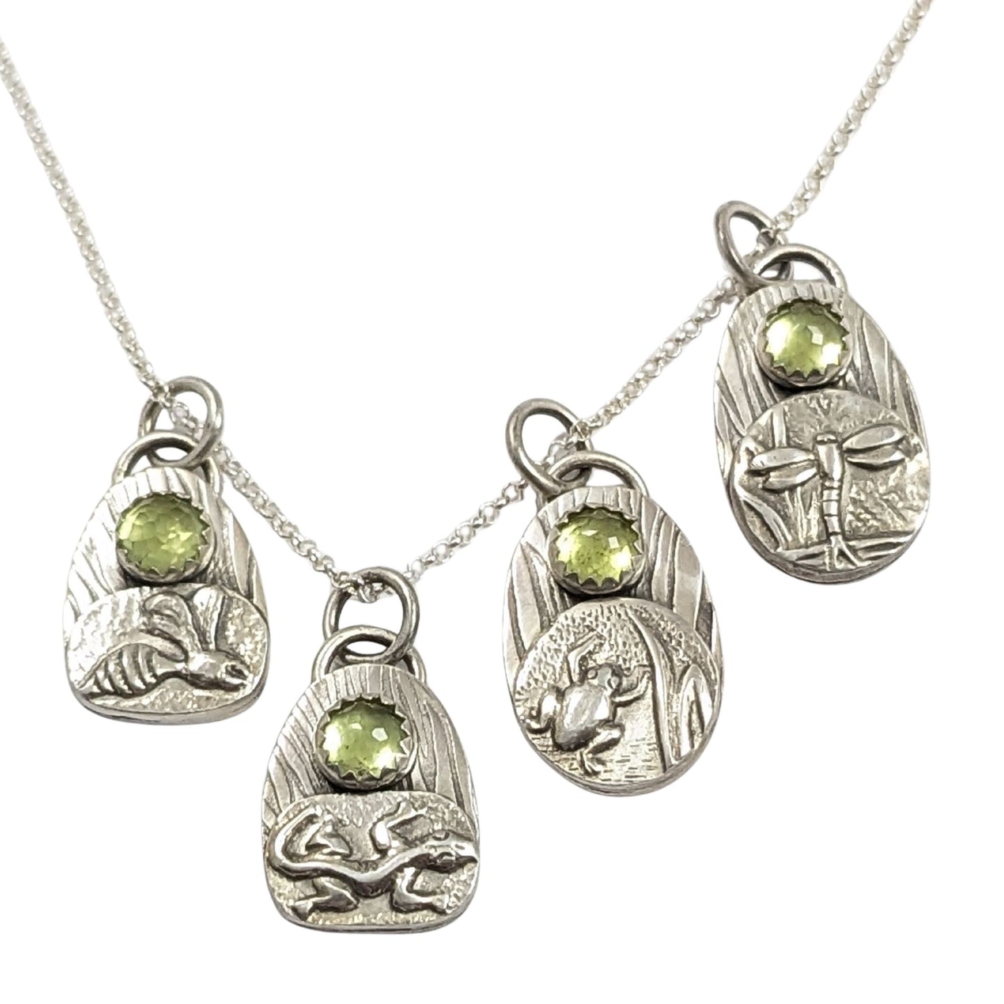 set of four sterling silver pendants with pond creatures. each has a reed-textured background and green peridot gemstone. Creatures are wasp, lizard, frog, dragonfly.