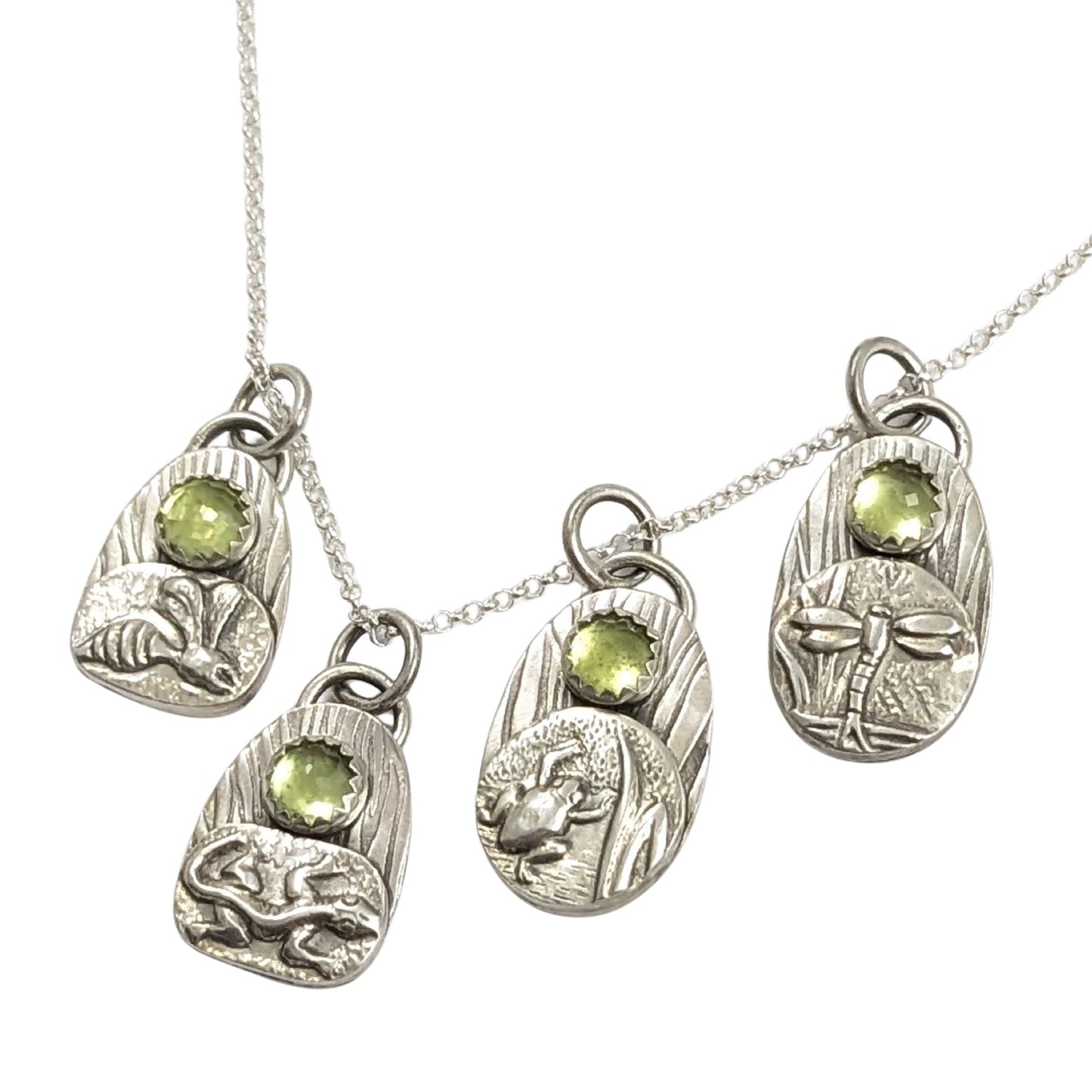 set of four sterling silver pendants with pond creatures. each has a reed-textured background and green peridot gemstone. Creatures are wasp, lizard, frog, dragonfly.