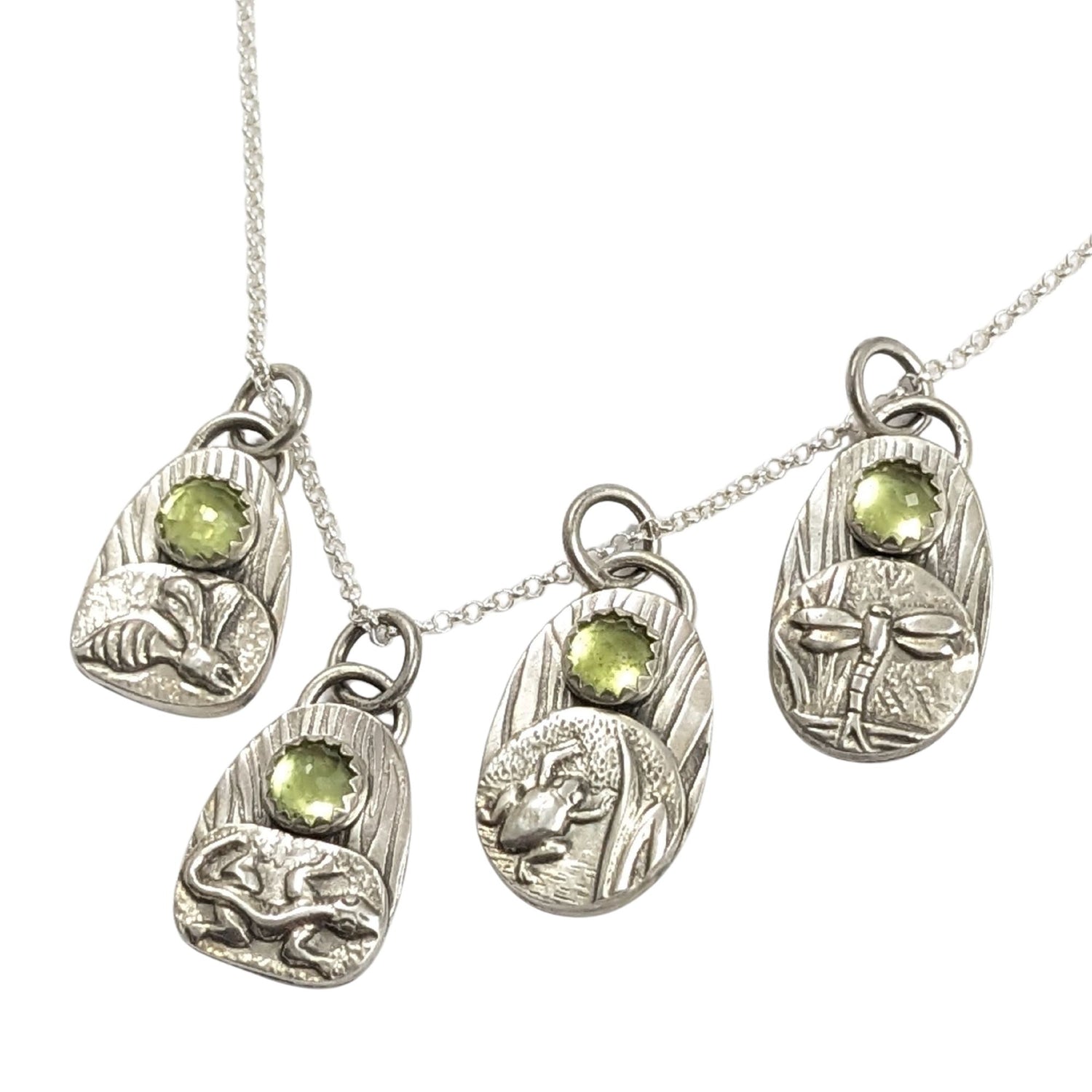 set of four sterling silver pendants with pond creatures. each has a reed-textured background and green peridot gemstone. Creatures are wasp, lizard, frog, dragonfly.