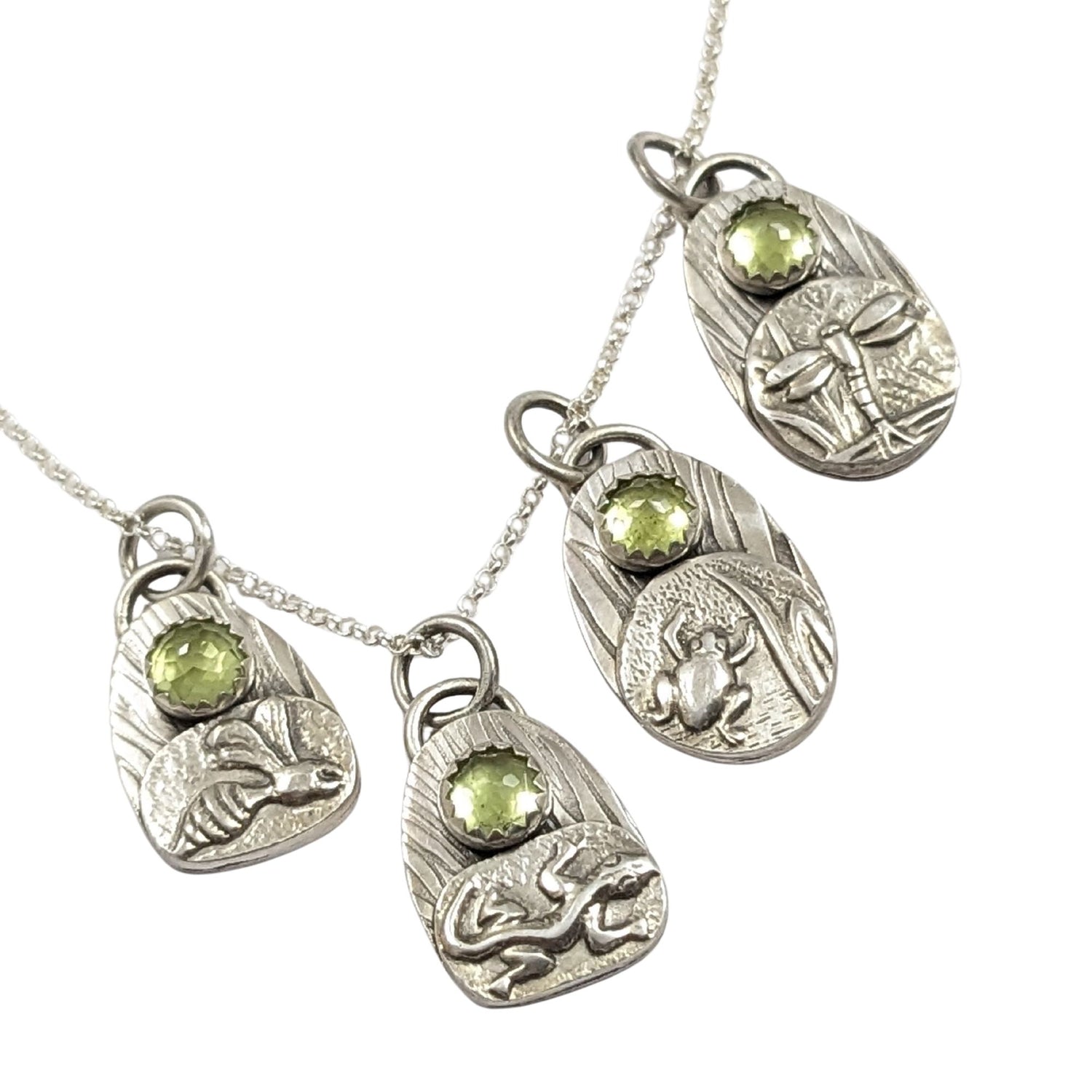 set of four sterling silver pendants with pond creatures. each has a reed-textured background and green peridot gemstone. Creatures are wasp, lizard, frog, dragonfly.