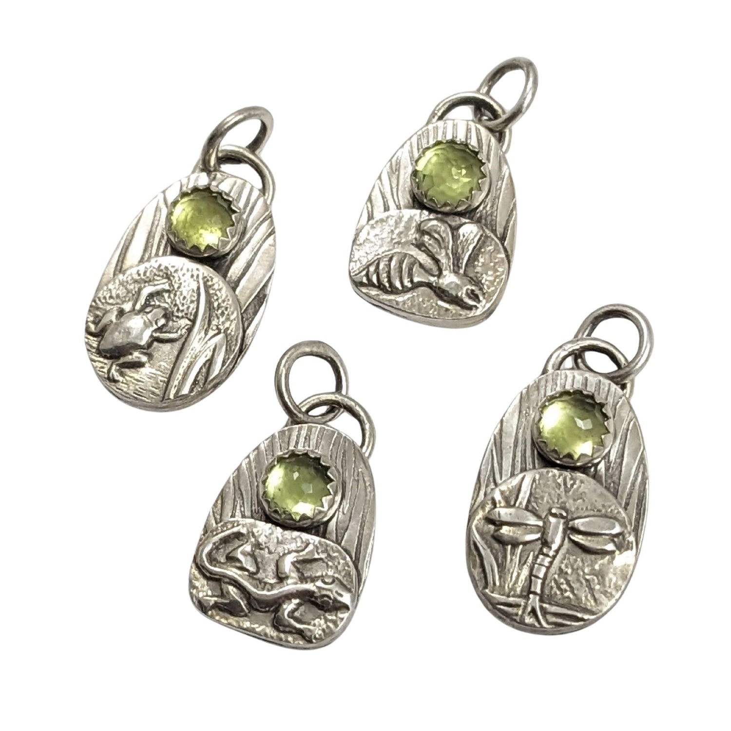 set of four sterling silver pendants with pond creatures. each has a reed-textured background and green peridot gemstone. Creatures are wasp, lizard, frog, dragonfly.