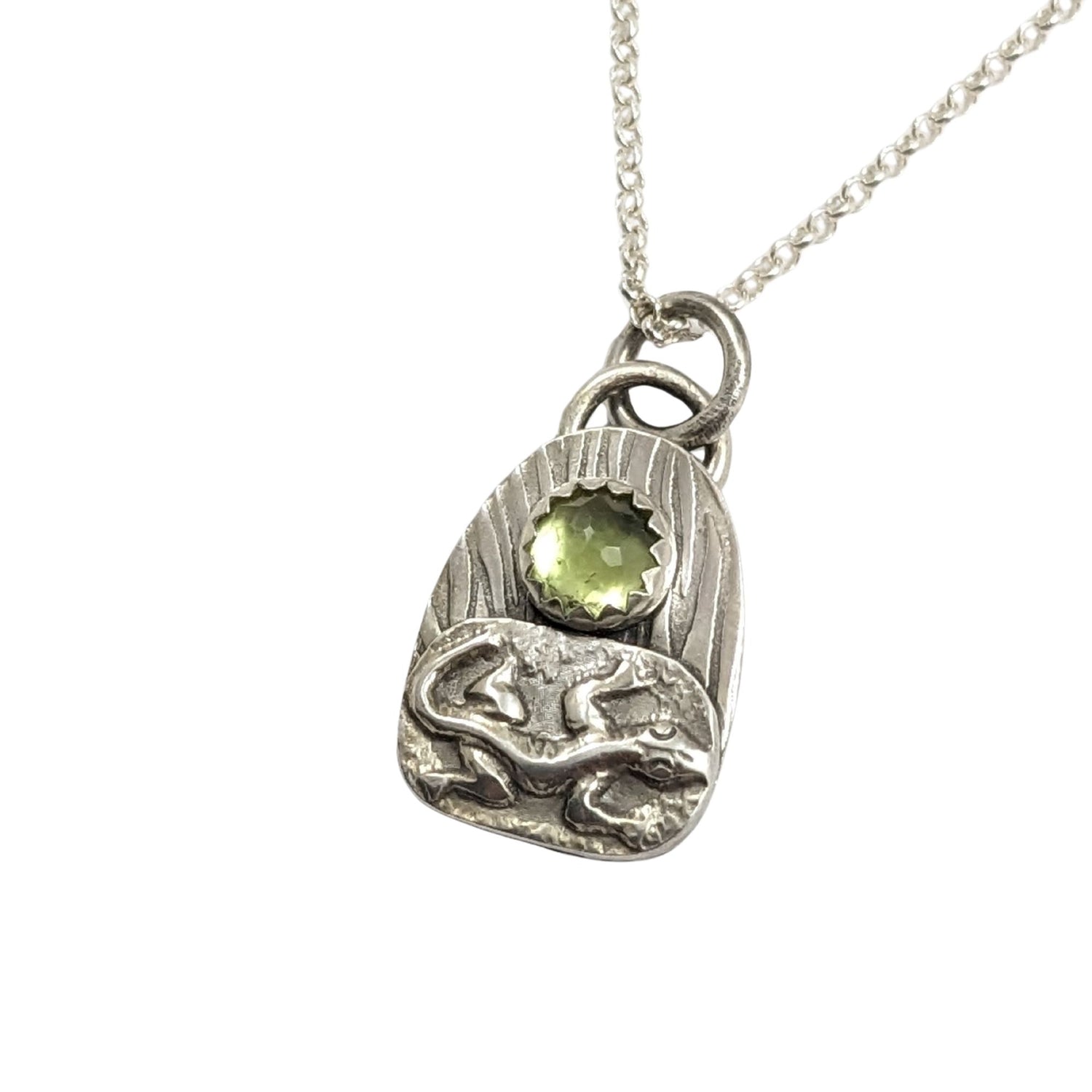 Lizard pendant from the set of four sterling silver pendants with pond creatures. each has a reed-textured background and green peridot gemstone. Creatures are wasp, lizard, frog, dragonfly.