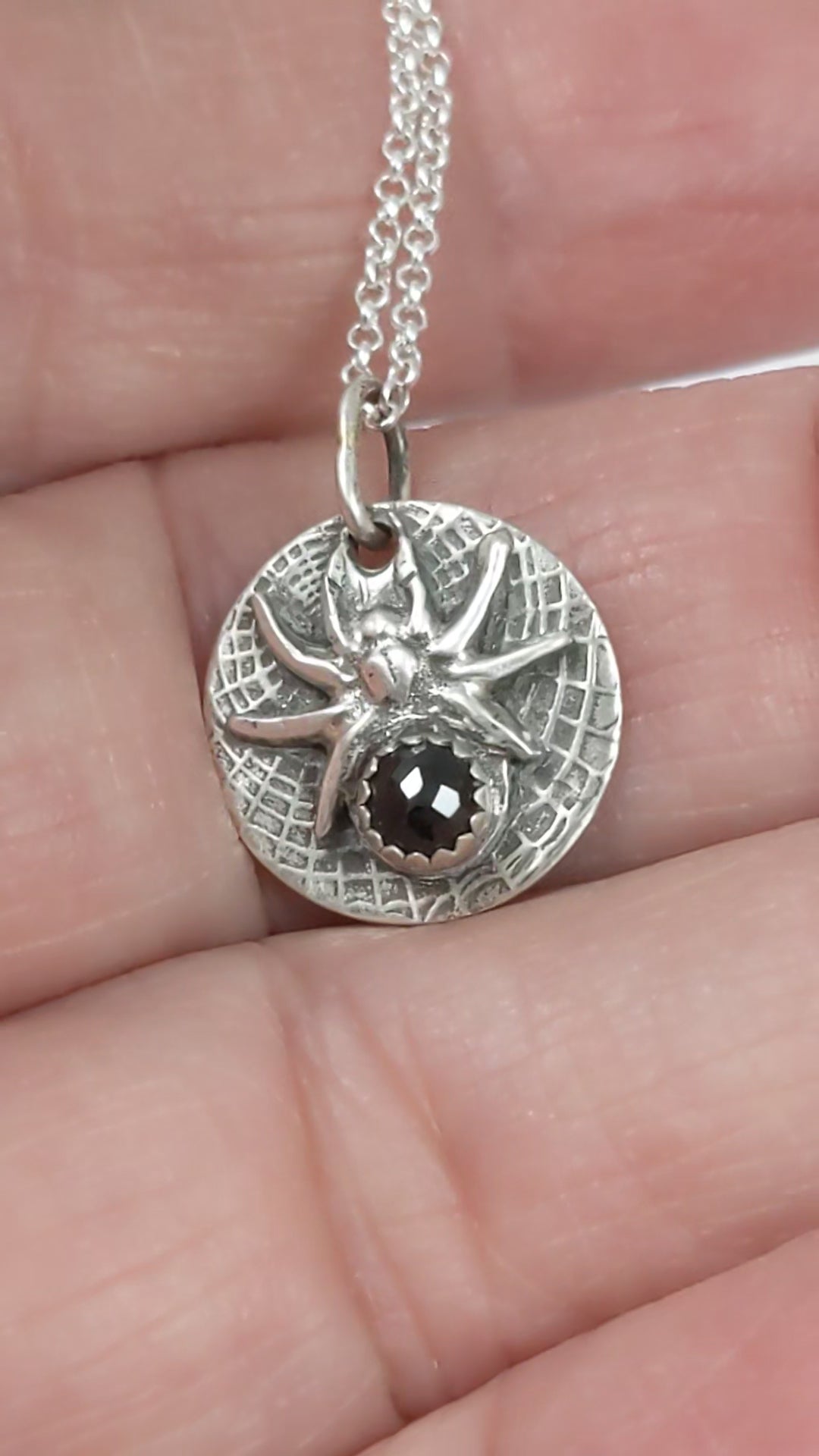 Round sterling silver pendant with a detailed black widow spider on a web texture background. The spider's body is a rose cut black onyx gemstone.