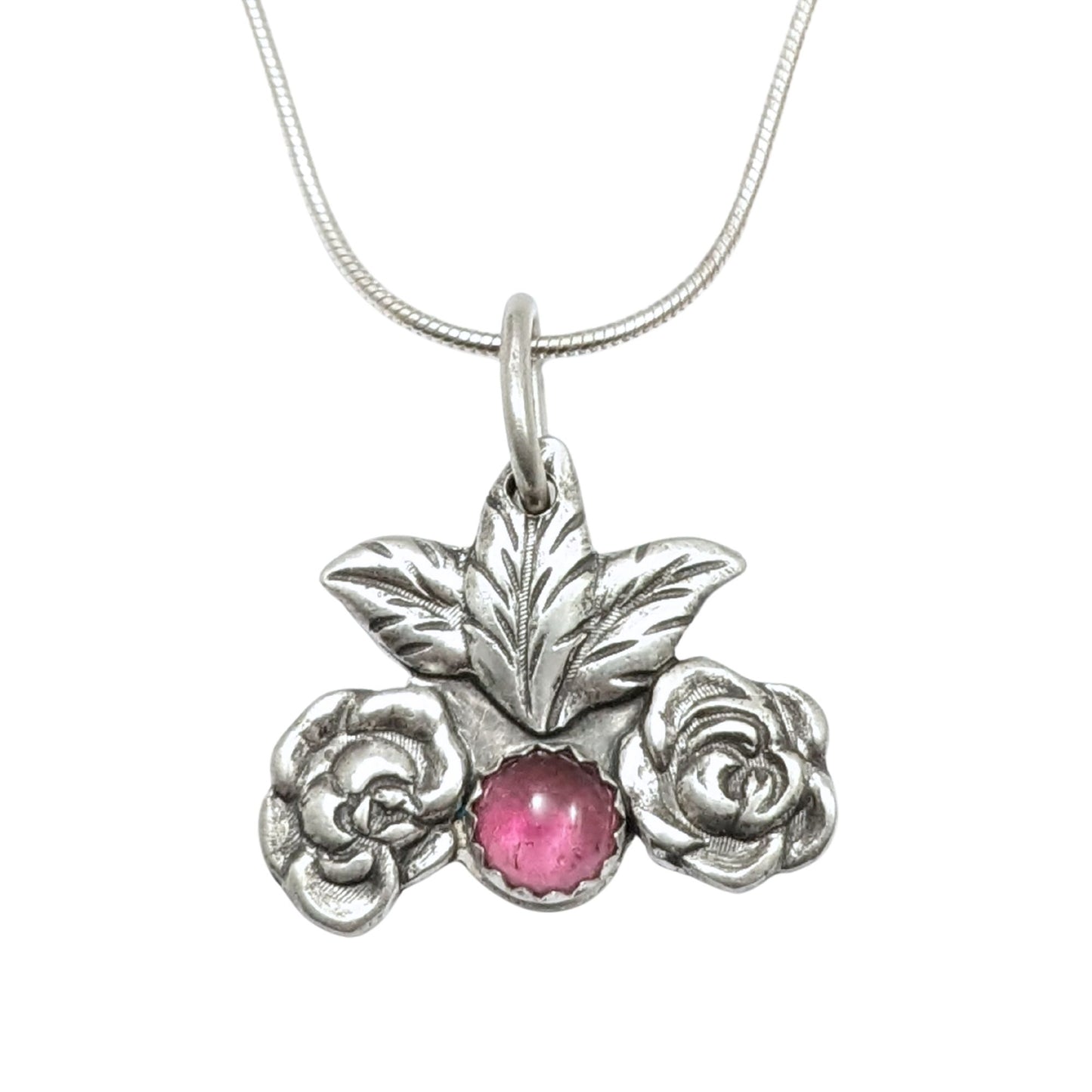 Silver pendant on a chain. At the bottom center there is a large pink tourmaline gemstone. There's a silver rose on each side of the gemstone and two leaves above it.
