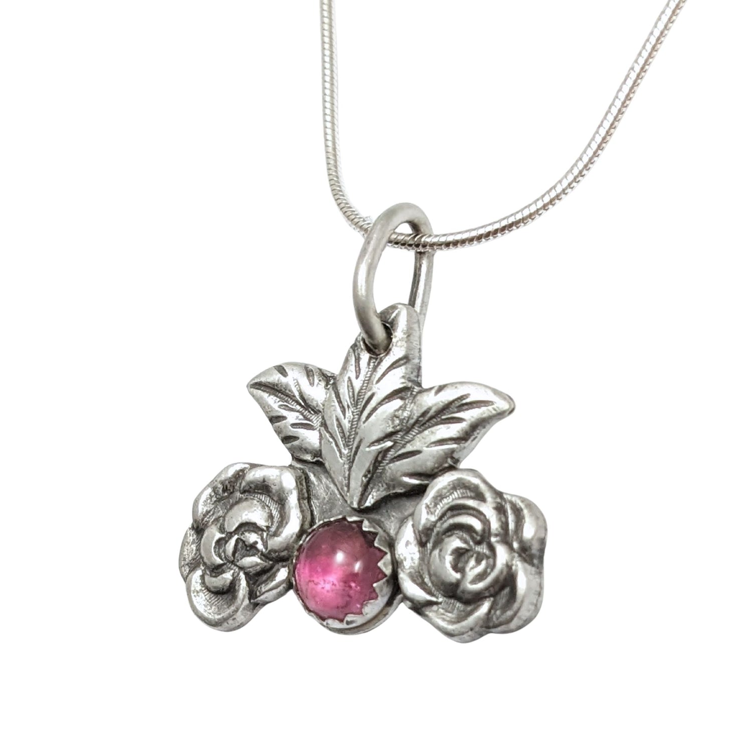 Silver pendant on a chain. At the bottom center there is a large pink tourmaline gemstone. There's a silver rose on each side of the gemstone and two leaves above it.