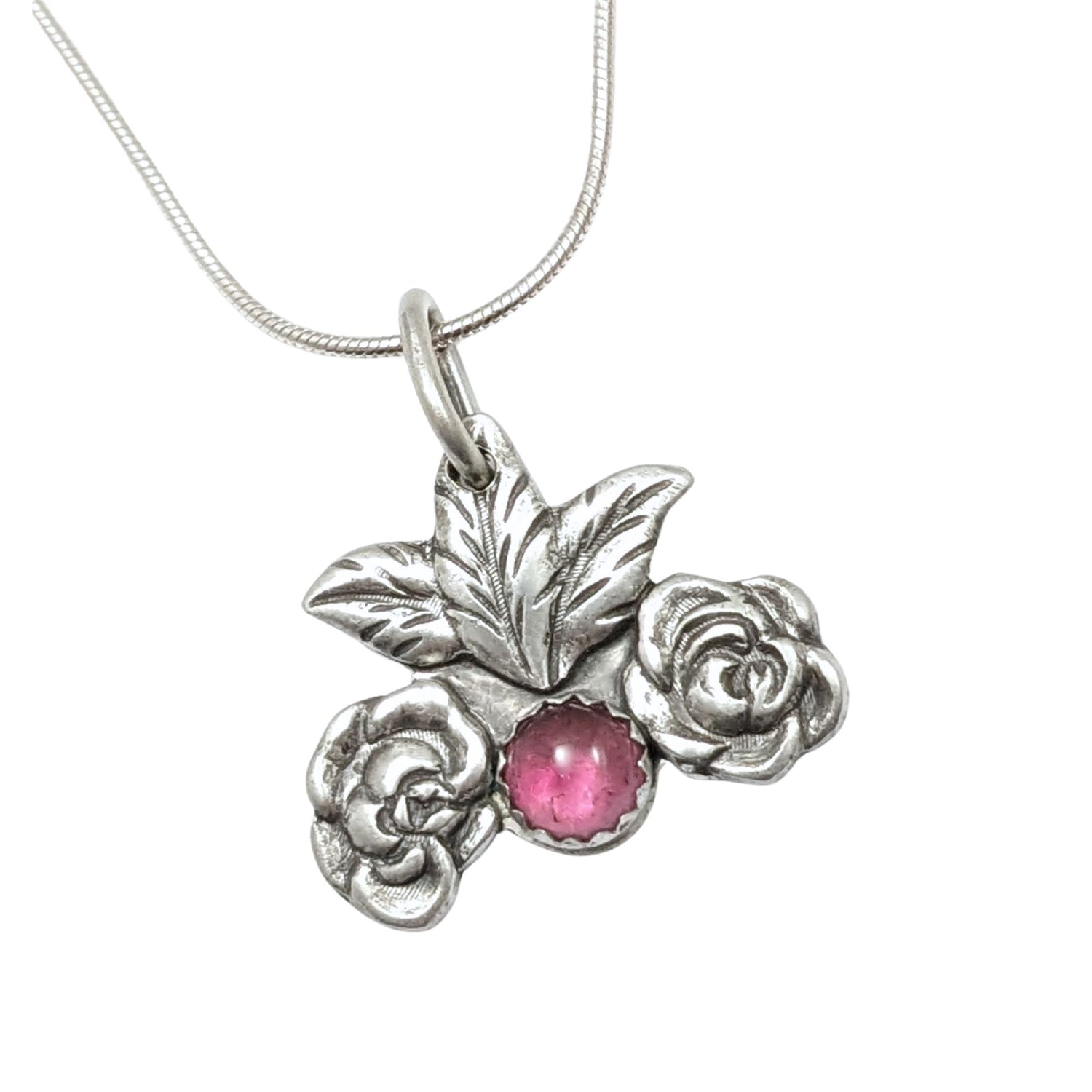 Silver pendant on a chain. At the bottom center there is a large pink tourmaline gemstone. There's a silver rose on each side of the gemstone and two leaves above it.