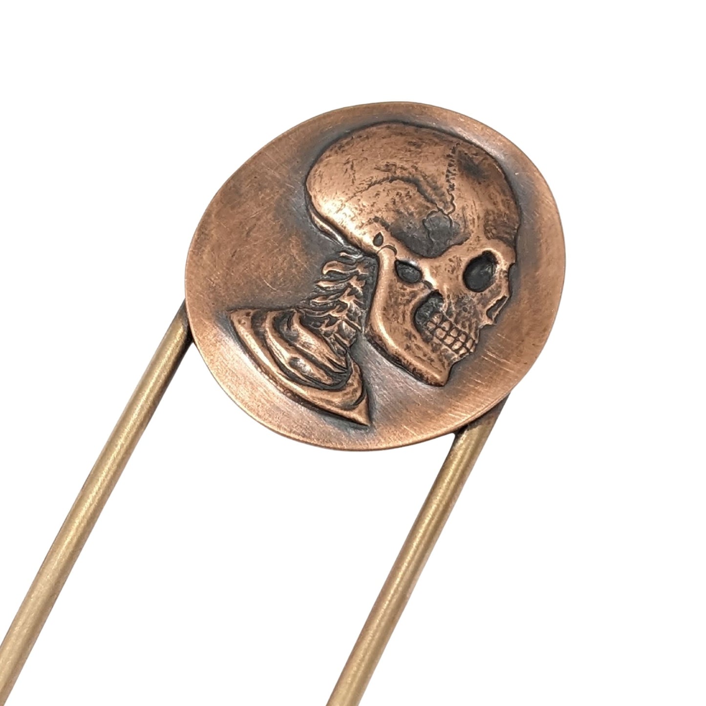 Raised image of a deeply detailed skull, including neck spine, on a round disk made of copper. The design is on a brass hair fork.
