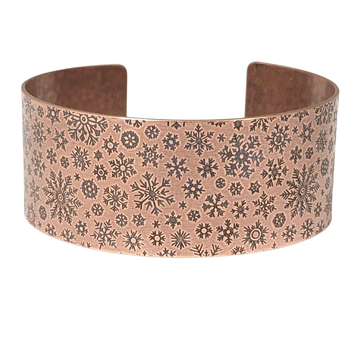 inch wide copper cuff bracelet with impressed design of different snowflake shapes. the impressions are oxidized, or blackened, to enhance the design