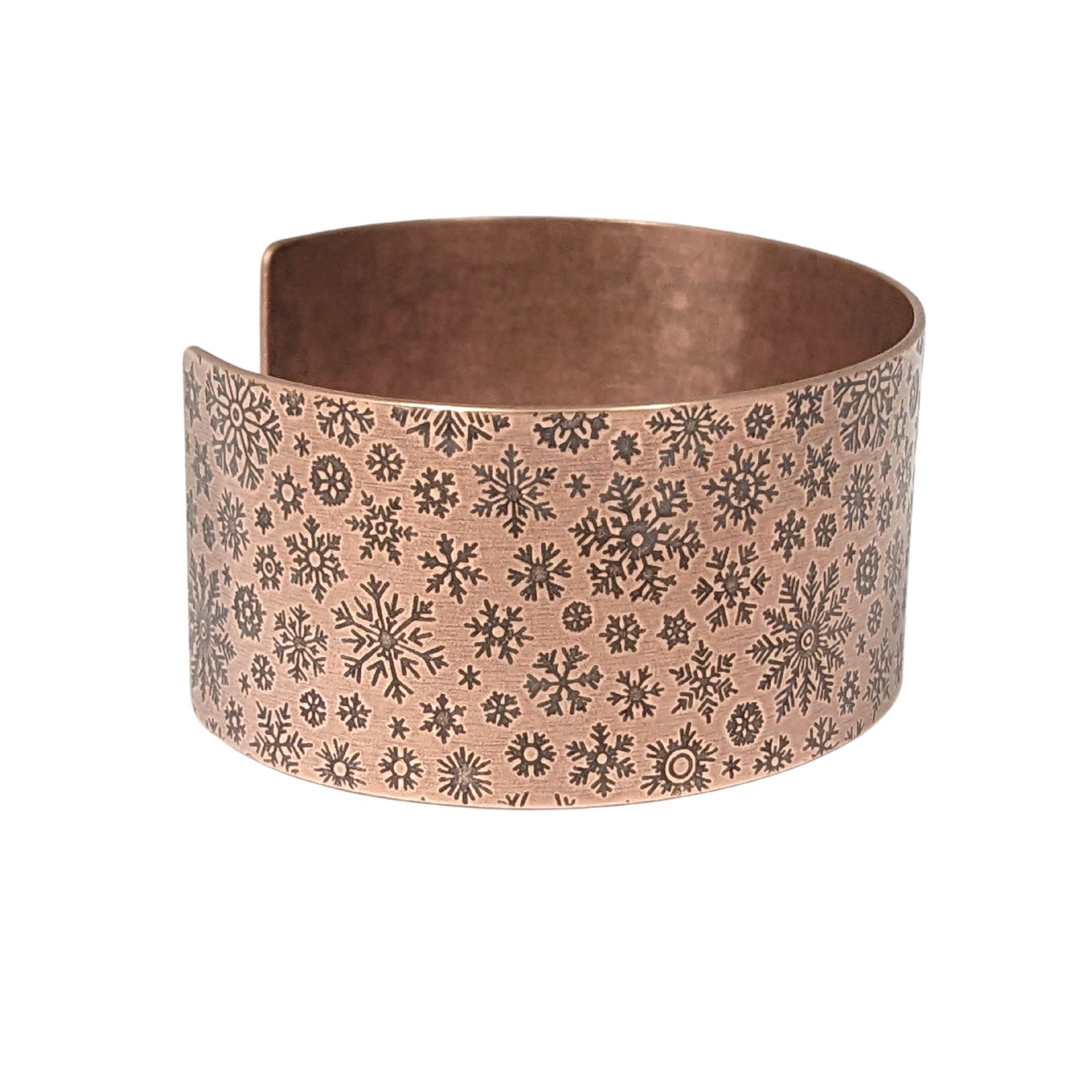 inch wide copper cuff bracelet with impressed design of different snowflake shapes. the impressions are oxidized, or blackened, to enhance the design