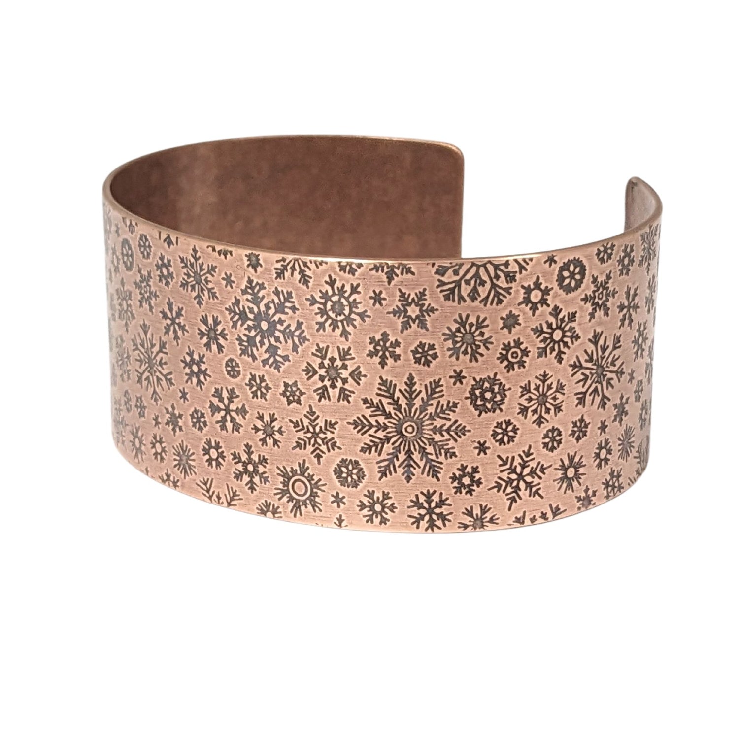 inch wide copper cuff bracelet with impressed design of different snowflake shapes. the impressions are oxidized, or blackened, to enhance the design