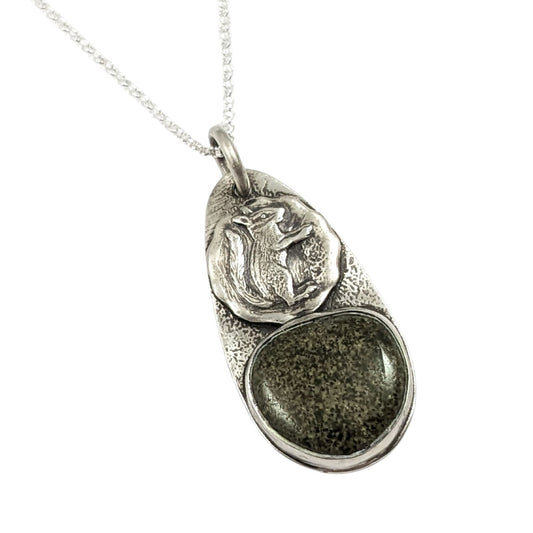 Oval sterling silver pendant. The top half has a circle with a raised image of a squirrel, the bottom half is a speckled green and tan stone.