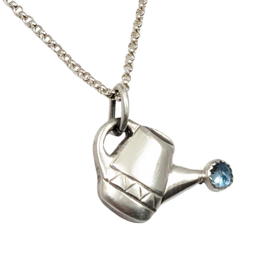 Sterling silver watering can pendant with a blue topaz gemstone at the end of the spout to represent water.