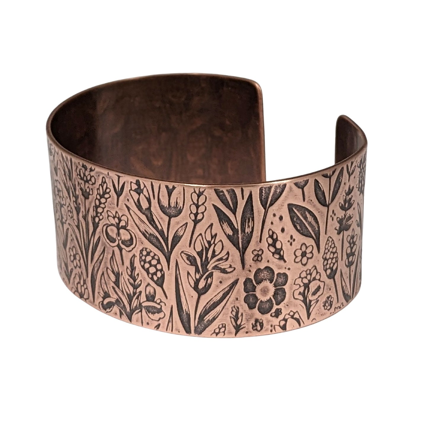 Inch wide copper cuff bracelet covered in impressed design of assorted wildflowers.