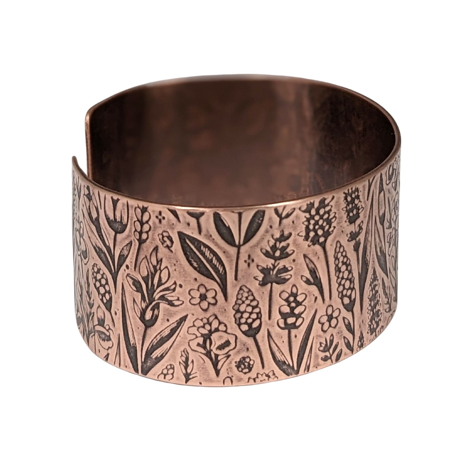 Inch wide copper cuff bracelet covered in impressed design of assorted wildflowers.